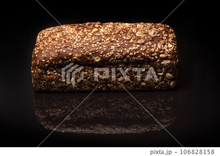 Loaf of fresh grain bread on black background, closeup. 106828158