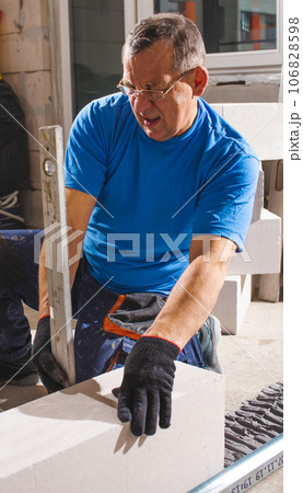 Happy smiling construction worker constructing or building wall by placing bricks and cement - concept of hard working, manual labour and daily wagers lifestyle 106828598