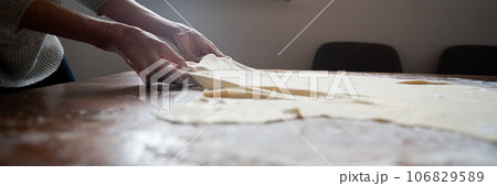 Female hands pulling homemade pastry dough for strudel Female hands pulling homemade pastry dough for strudel 106829589