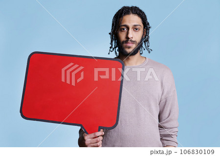 Arab man holding red empty banner with place for text for advertising mock up and looking at camera. Model standing with blank dialog frame for message with copy space portrait Arab man holding red empty banner with place for text for advertising mock up and looking at camera. Model standing with blank dialog frame for message with copy space portrait 106830109