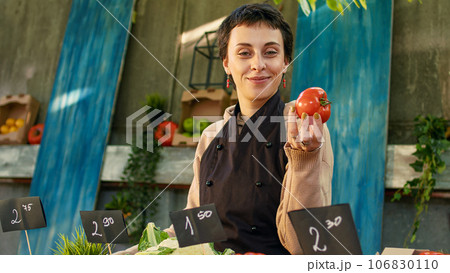 Young greengrocer with apron showing organic farming produce, arranging colorful bio fruits and veggies on stand. Small business farmers market owner selling natural fresh products. Young greengrocer with apron showing organic farming produce, arranging colorful bio fruits and veggies on stand. Small business farmers market owner selling natural fresh products. 106830110
