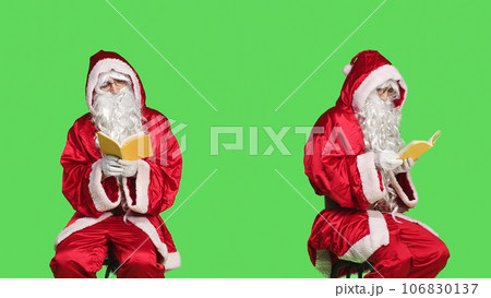Santa reads literature sitting on chair, man wearing festive red costume while he is reading poetry book over greenscreen backdrop. Father christmas enjoying fairytale story, winter holiday. Santa reads literature sitting on chair, man wearing festive red costume while he is reading poetry book over greenscreen backdrop. Father christmas enjoying fairytale story, winter holiday. 106830137