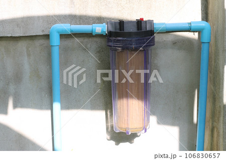 The single stage water filter is mounted on a blue PVC plastic water pipe that is attached to the wall. 106830657