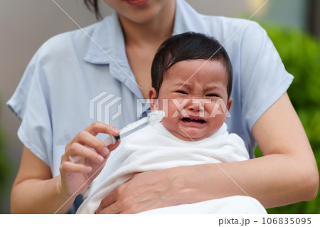 mother making nasal wash for crying infant with syringe and saline. cleaning baby nose 106835095