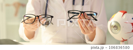 Ophthalmologist holds different eyeglasses in her hands while sitting at desk in medical clinic. Ophthalmologist holds different eyeglasses in her hands while sitting at desk in medical clinic. 106836580