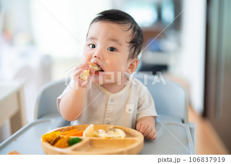 離乳食後期でをつかみ食べをしてご機嫌な生後9か月の赤ちゃん 106837919