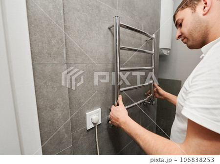 Male worker hanging electric heated towel rack on the wall in bathroom. Man installing stainless steel bath towel heater in apartment under renovation. Home renovation concept. Male worker hanging electric heated towel rack on the wall in bathroom. Man installing stainless steel bath towel heater in apartment under renovation. Home renovation concept. 106838253