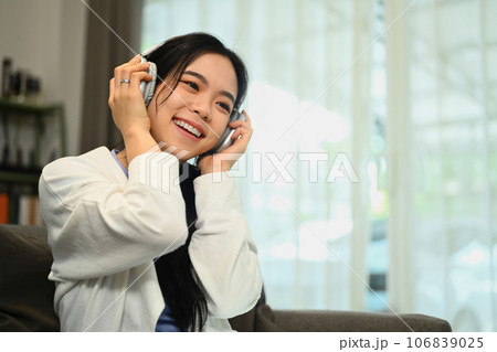 Relaxed young woman enjoying favorite track, listening to music through headphones while sitting in living room 106839025