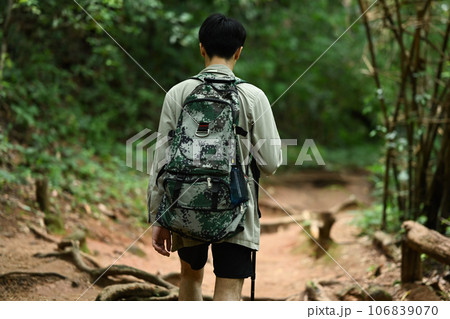Back view of man tourist with backpack and trekking pole walking along the forest path. Traveling and adventure concept Back view of man tourist with backpack and trekking pole walking along the forest path. Traveling and adventure concept 106839070