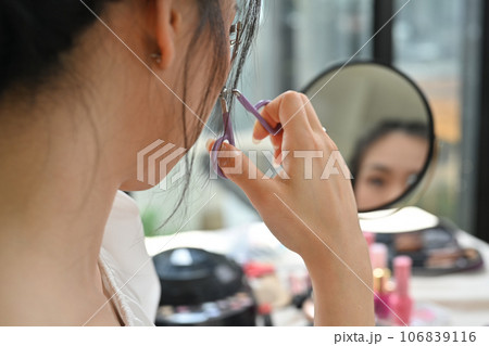 Young woman using eyelash curler curling eyelashes before mascara in front of mirror 106839116
