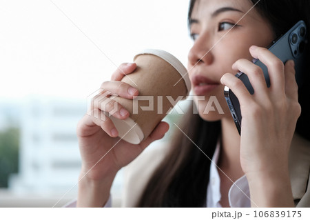 Beautiful millennial businesswoman drinking coffee from paper cup and talking on mobile phone 106839175