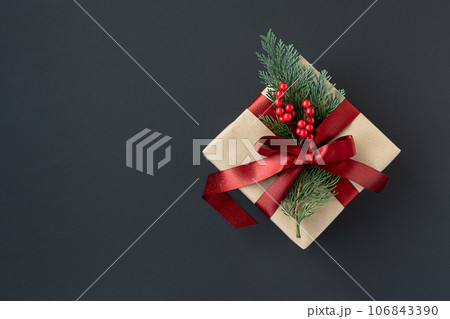 Banner with craft gift box with red ribbon and thuja sprig on a dark background. Banner with craft gift box with red ribbon and thuja sprig on a dark background. 106843390