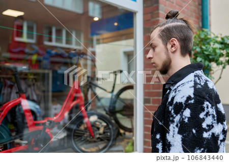 Young male looking dreamily at modern bicycles in shop window Young male looking dreamily at modern bicycles in shop window 106843440