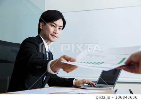 オフィスでパソコンを操作しながら会議をする若い男性のビジネスマン 106843636