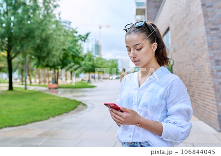 Portrait of young teenage female with smartphone, on street of modern city 106844045