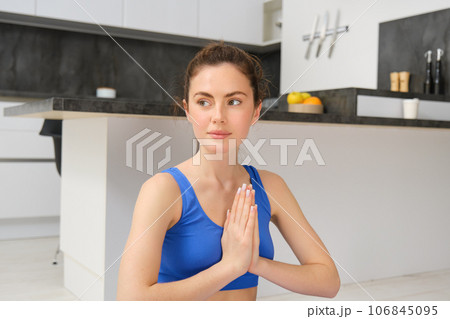 Young healthy beautiful woman in sports top and leggings practicing yoga at home, sitting in lotus position on yoga mat, meditating, smiling, relaxed, eyes closed, meditation concept Young healthy beautiful woman in sports top and leggings practicing yoga at home, sitting in lotus position on yoga mat, meditating, smiling, relaxed, eyes closed, meditation concept 106845095