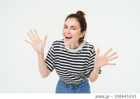 Image of happy, beautiful young woman makes jazz hands, surprise gesture, posing in casual t-shirt and jeans over white background 106845243