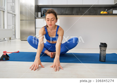 Portrait of woman stretching her legs before workout exercises, doing fitness training on yoga rubber mat, does sport from home 106845274