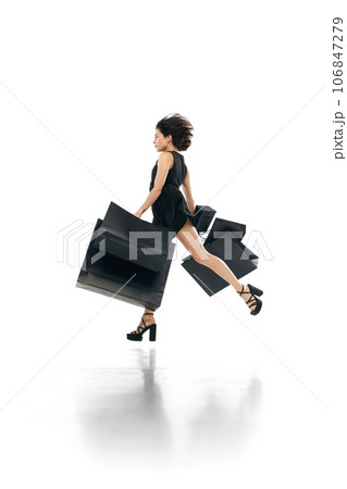 Black friday concept. Shopaholic. Side view portrait of woman wearing fashion mini black dress flying, running to shopping mall. 106847279