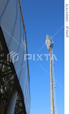 a high floodlight mast and a fragment of the stadium structure against the blue sky, elements of urban sports infrastructure and architecture, part of the stadium with lighting equipment 106847479
