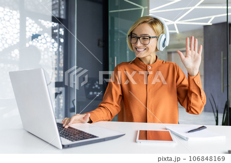 Young joyful woman at workplace listens to music in headphones, businesswoman dances and sings, sitting at work table inside office, female programmer well done successf technical project celebrates. 106848169