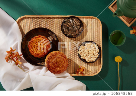 Bamboo tray with mooncakes and dishes of pumpkin seeds and sunflower seeds arranged on. Green background. Mid-Autumn Festival Food Advertising 106848568