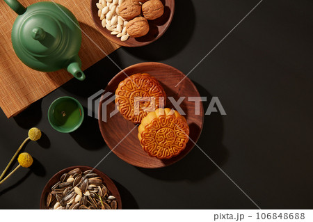 Delicious mooncakes, set of tea and dry nuts on black background. Mid-Autumn Festival is also known as Moon Festival or Lantern Festival according to the lunar calendar. Blank space for design Delicious mooncakes, set of tea and dry nuts on black background. Mid-Autumn Festival is also known as Moon Festival or Lantern Festival according to the lunar calendar. Blank space for design 106848688