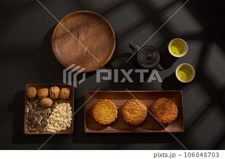Top view of wooden trays containing mooncakes and different seeds decorated on black background. Chinese Mid-Autumn Festival concept. Advertising photo Top view of wooden trays containing mooncakes and different seeds decorated on black background. Chinese Mid-Autumn Festival concept. Advertising photo 106848703