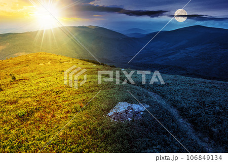 narrow path through grassy meadow among white stones on top of the hill in high mountain with sun and moon at twilight. day and night time change concept. mysterious nature scenery in morning light 106849134