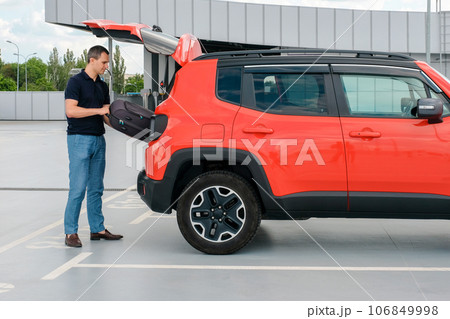 A man in a parking lot puts his suitcase in the trunk of a car. A man in a parking lot puts his suitcase in the trunk of a car. 106849998