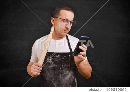 Male chef in apron using phone on dark background. Cooking concept 106850062