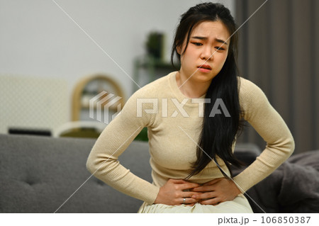 Young woman sitting on sofa at home suffering from stomachache, diarrhea or indigestive problem. Health care concept 106850387