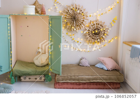 The interior of a children's room decorated for the Christmas holidays. Soft mattresses with garlands in the form of stars and a children's wardrobe with soft pillows. The interior of a children's room decorated for the Christmas holidays. Soft mattresses with garlands in the form of stars and a children's wardrobe with soft pillows. 106852057