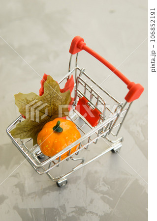 Grocery cart with decorative pumpkins and maple leaves on a concrete background. The concept of the autumn sales. Black Friday and cyber Monday. Grocery cart with decorative pumpkins and maple leaves on a concrete background. The concept of the autumn sales. Black Friday and cyber Monday. 106852191