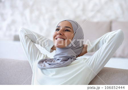 Happy young muslim woman in hijab sitting relaxed on sofa at home and resting. Satisfied with a successful day. Happy young muslim woman in hijab sitting relaxed on sofa at home and resting. Satisfied with a successful day. 106852444