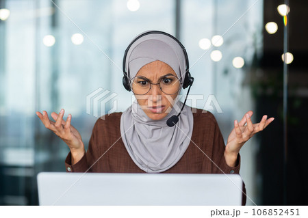 Close-up photo. Serious and strict and demanding Muslim female teacher in hijab and headset explaining and teaching online via laptop. Close-up photo. Serious and strict and demanding Muslim female teacher in hijab and headset explaining and teaching online via laptop. 106852451