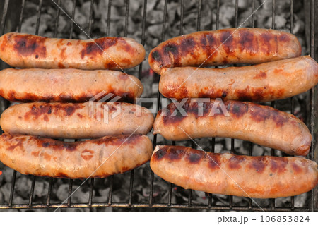 Grilled sausages. Cook man preparing grilling food bbq. Barbecue with smoke, flame outdoors. Tasty juicy german bratwurst. Charcoal kettle grill outside in backyard. Family summer vacation. Close-up Grilled sausages. Cook man preparing grilling food bbq. Barbecue with smoke, flame outdoors. Tasty juicy german bratwurst. Charcoal kettle grill outside in backyard. Family summer vacation. Close-up 106853824