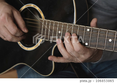 Playing the guitar. Strumming black acoustic guitar. Musician plays music. Man fingers holding mediator. Male hand playing guitar neck in dark room. Unrecognizable person rehearsing, fretboard closeup Playing the guitar. Strumming black acoustic guitar. Musician plays music. Man fingers holding mediator. Male hand playing guitar neck in dark room. Unrecognizable person rehearsing, fretboard closeup 106853865