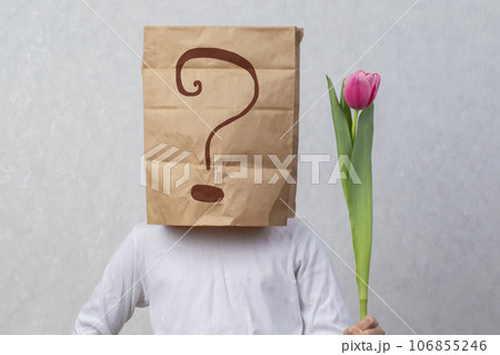 An anonymous man with a box on his head that limits his identity holds a flower. Hidden emotions. A gift from a stranger. An anonymous man with a box on his head that limits his identity holds a flower. Hidden emotions. A gift from a stranger. 106855246