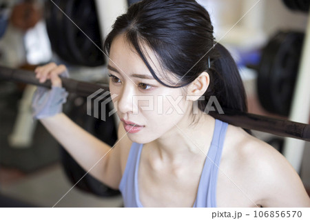 フィットネスジムでバーベルスクワットをする若い女性 106856570