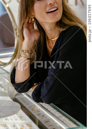 Charming long haired caucasian woman choosing jewellery in a modern jewelry store greeting visitors and cliently hospitably. Positive people in small business concept. Charming long haired caucasian woman choosing jewellery in a modern jewelry store greeting visitors and cliently hospitably. Positive people in small business concept. 106857695