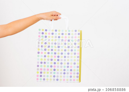 Closeup women hand holding a white circular pattern shopping bag, studio shot isolated on white background, female holds in hand white clear empty blank craft paper gift bag for purchases Closeup women hand holding a white circular pattern shopping bag, studio shot isolated on white background, female holds in hand white clear empty blank craft paper gift bag for purchases 106858886
