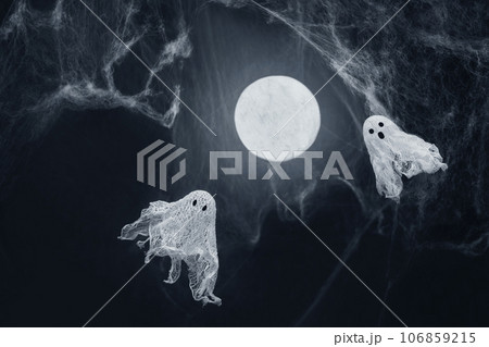 Ghosts of gauze on a dark background with a glowing moon and spiderwebs. Creative DIY Halloween decor. Halloween greeting card. Copy space. Ghosts of gauze on a dark background with a glowing moon and spiderwebs. Creative DIY Halloween decor. Halloween greeting card. Copy space. 106859215