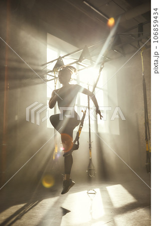 Professional training. Full-length of young athletic woman in sports clothing training legs with trx fitness straps in the gym. 106859434
