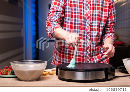 Woman cooking delicious crepe on electric pancake maker in kitchen, closeup Woman cooking delicious crepe on electric pancake maker in kitchen, closeup 106859711