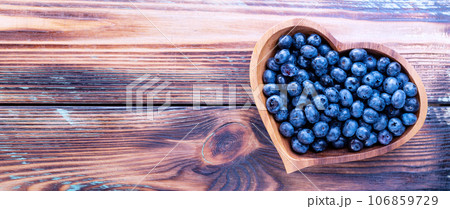 Freshly picked blueberries in a heart-shaped wooden plate on a wooden table, top view 106859729