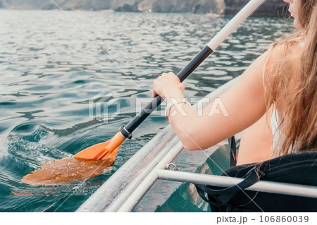 Woman in kayak back view. Happy young woman with long hair floating in transparent kayak on the crystal clear sea. Summer holiday vacation and cheerful female people relaxing having fun on the boat Woman in kayak back view. Happy young woman with long hair floating in transparent kayak on the crystal clear sea. Summer holiday vacation and cheerful female people relaxing having fun on the boat 106860039