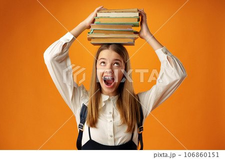 Teen schoolgirl holding stack of books over head on yellow background Teen schoolgirl holding stack of books over head on yellow background 106860151