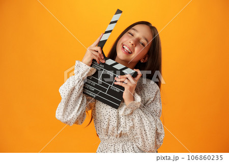 Happy smiling girl portrait holding clapper board on yellow background 106860235