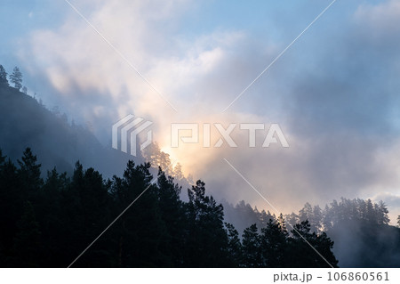 Mountains and peaks in fog at sunrise or sunset. Sun from behind the mountain. Amazing view of mountains and forest landscape with cloudy skies Altai mountains. Mountains and peaks in fog at sunrise Mountains and peaks in fog at sunrise or sunset. Sun from behind the mountain. Amazing view of mountains and forest landscape with cloudy skies Altai mountains. Mountains and peaks in fog at sunrise 106860561